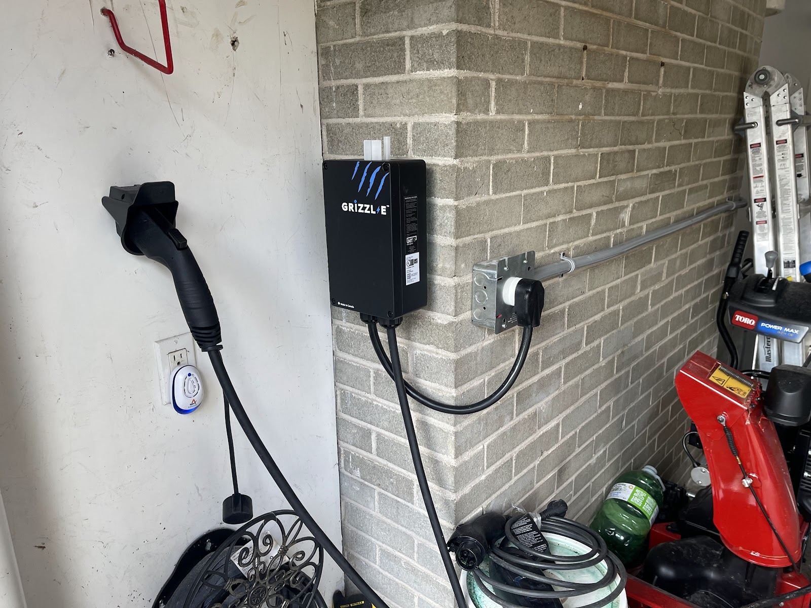 A black EV charger mounted on a garage wall with its cable and plug
